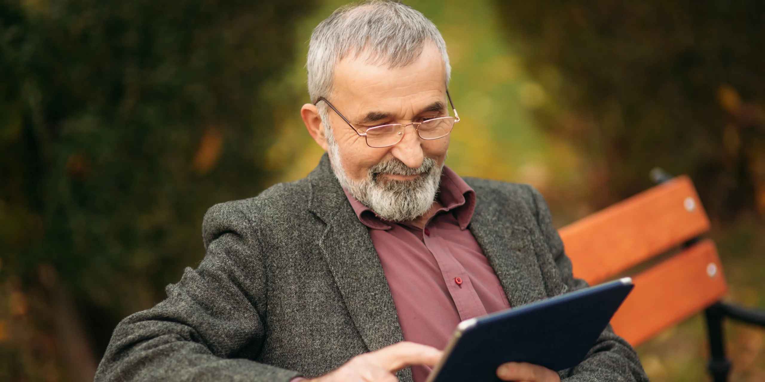 Préretraité suivant une formation sur une tablette. Cet homme est assis sur un banc dans un parc.