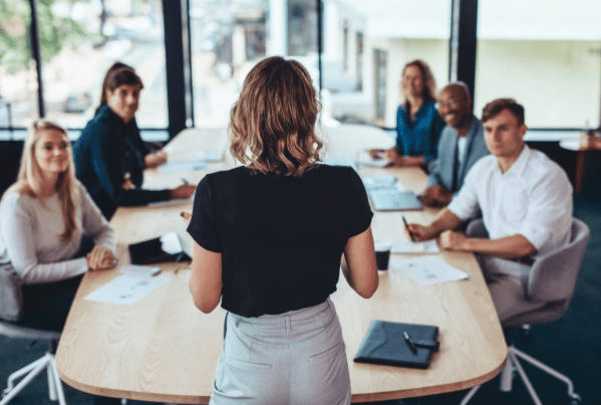Un groupe de personne suit une formation en entreprise autour d'une table dans une salle de réunion tout en bénéficiant des avantages de la formation en entreprise.