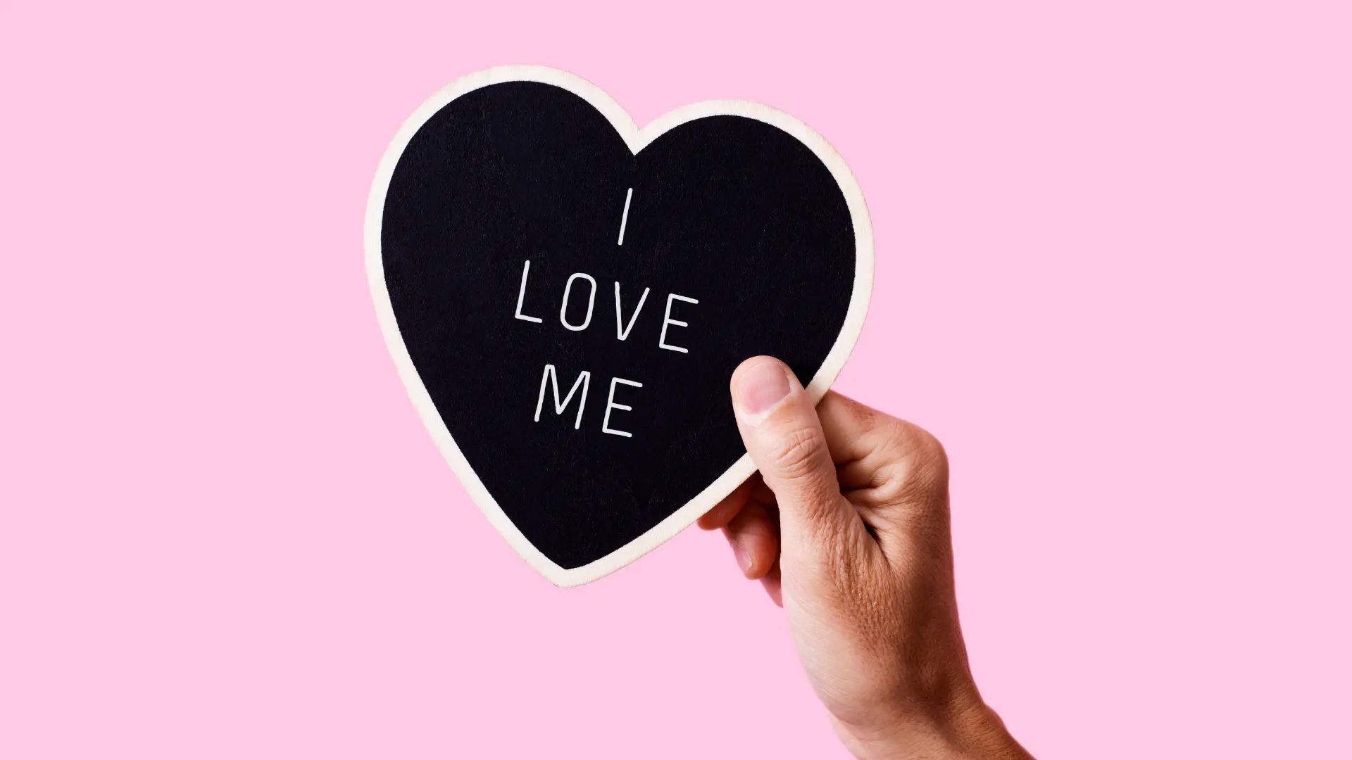 Une main tient un cœur en papier sur lequel il est écrit "i love me" pour mettre en avant la confiance en soi.