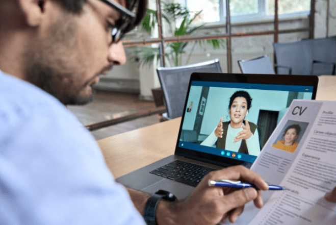 Recruteur faisant passer un entretien à un candidat en visio. Le recruteur regarde le cv du candidat pour lui poser des questions.