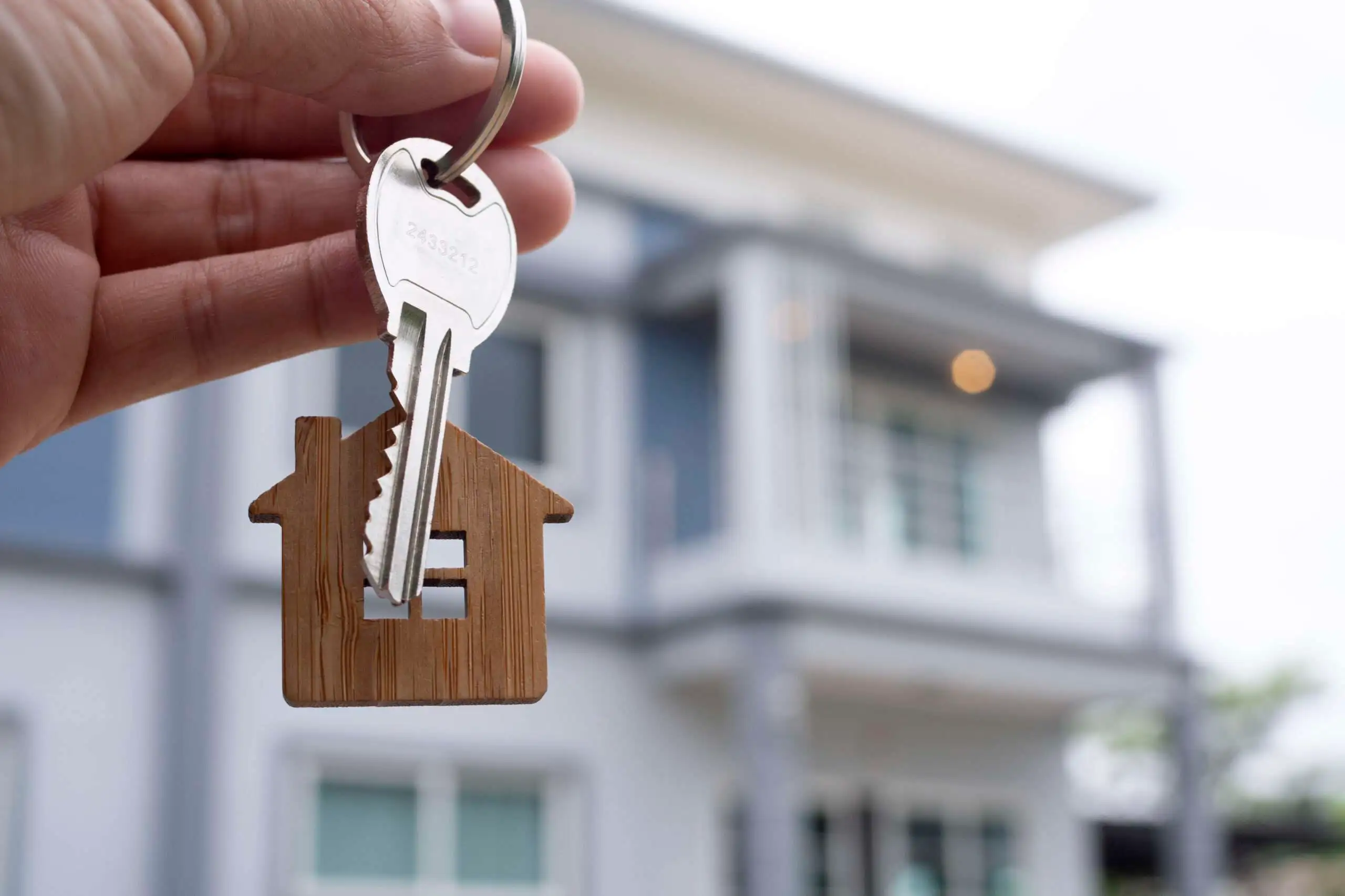Une main tenant une clé devant une maison, pour illustrer l'image d'une personne ayant investit dans l'immobilier.