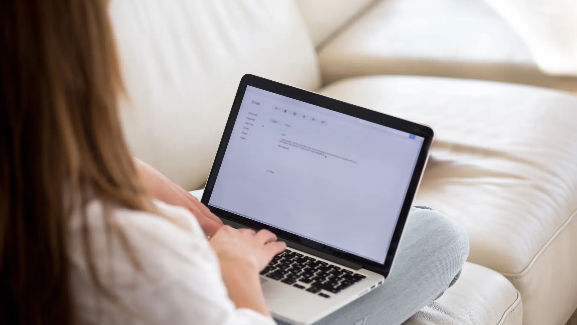 Une femme, assise sur son lit écrivant une lettre de motivation sur son ordinateur portable.