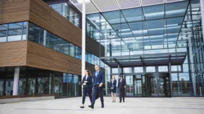 Groupe de personne marchant devant leur immeuble, probablement leur entreprise. L'image montre des employés se rendant à une formation grâce au financement des formations pour les entreprises par les opco que leur organisation a obtenu.